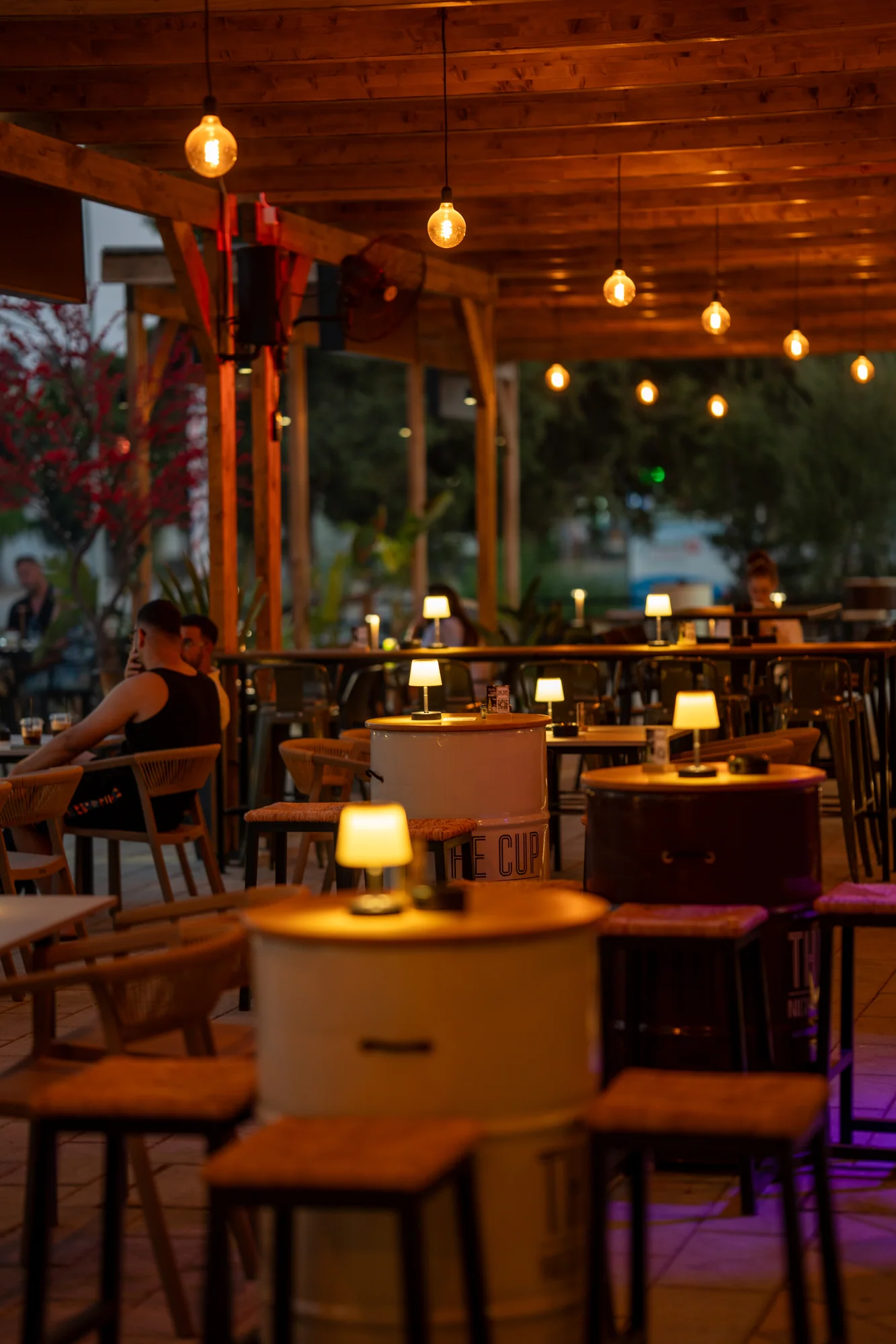 The Cup terrace with barrel tables and glowing lamps at dusk