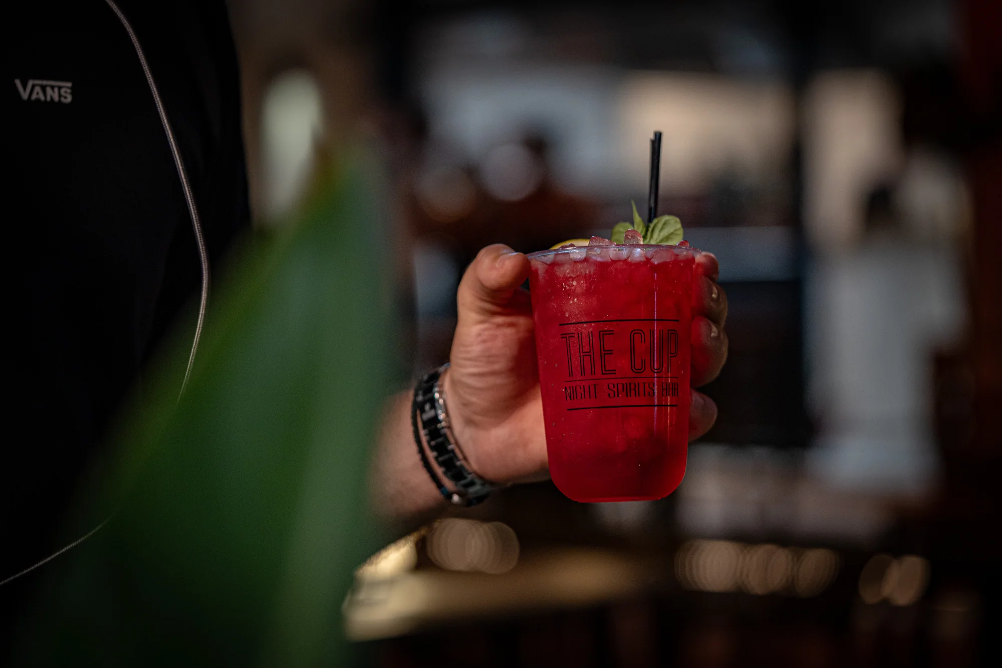 A red drink with mint and a citrus garnish in a The Cup branded cup